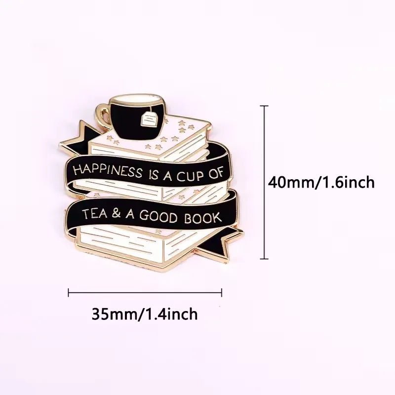 The Kiss Me Later enamel pin features a stack of books with a tea cup, wrapped in a banner reading Happiness is a cup of tea & a good book. Measures 40mm tall by 35mm wide.