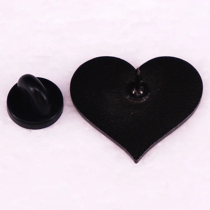 A 1-inch black heart-shaped enamel pin shown with its butterfly clutch backing detached on a white surface.