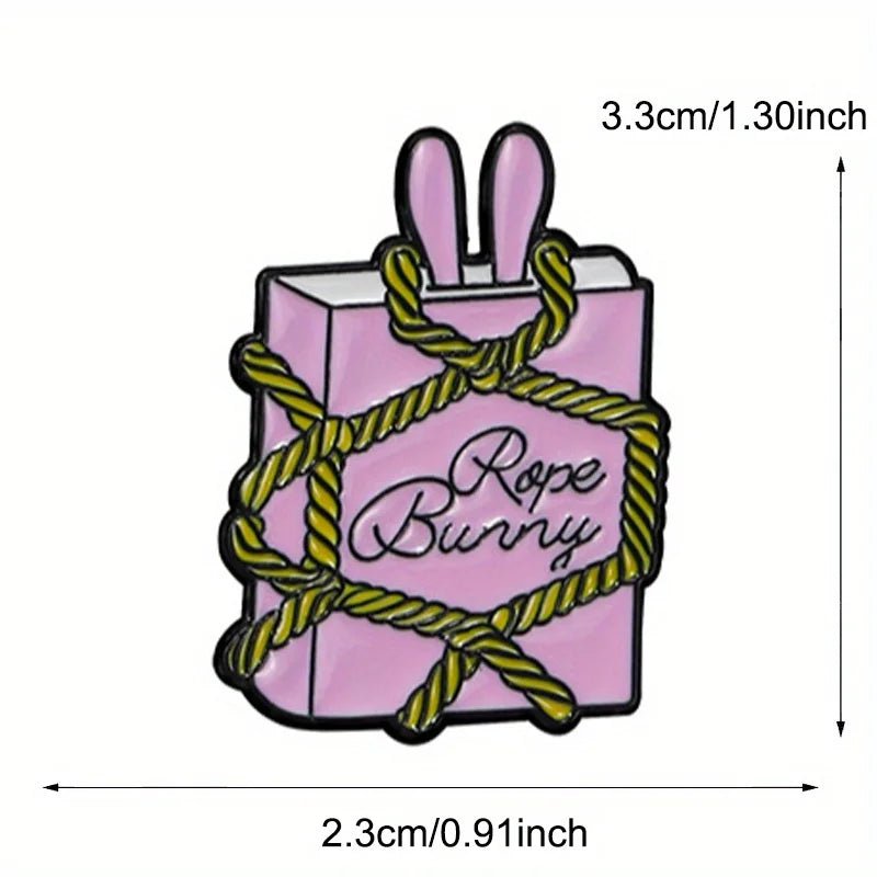 A pink box with bunny ears, “Rope Bunny” text, and yellow rope. This enamel pin is 3.3 cm tall by 2.3 cm wide