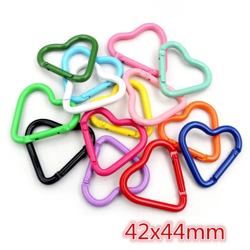 A pile of colorful, heart-shaped rainbow carabiners from My Cutesy Era, size 42x44mm (noted in red text). The perfect queer accessory to express love and pride.