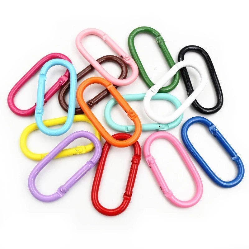 A scattered pile of My Cutesy Era rainbow carabiners in red, blue, green, yellow, pink, white, black, and purple oval-shaped clips displayed on a white background.