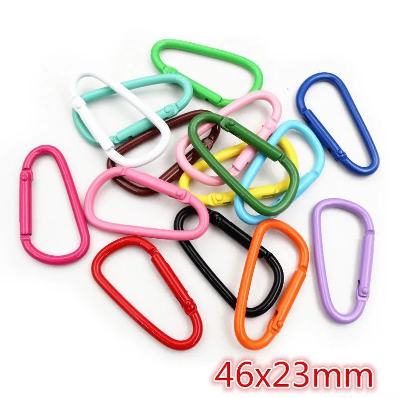 A pile of colorful My Cutesy Era rainbow carabiners in pink, red, blue, green, yellow, and black is shown. The 46x23mm size appears in red text—perfect as a fun queer accessory for the wlw community.