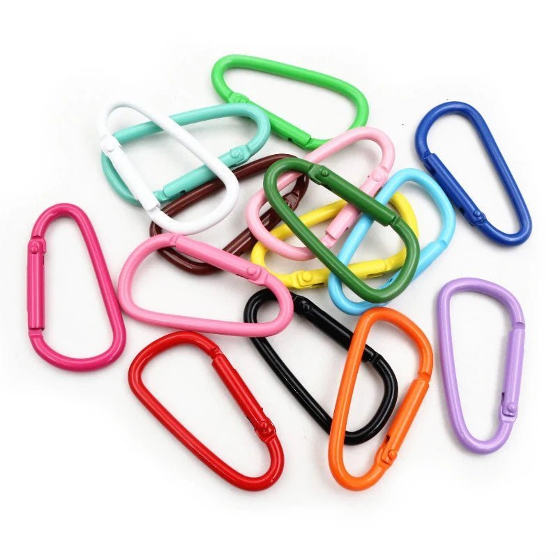A pile of colorful My Cutesy Era rainbow carabiners in various shapes and shades—red, pink, green, blue, orange, black—scattered on a white background, perfect as a bold queer accessory.