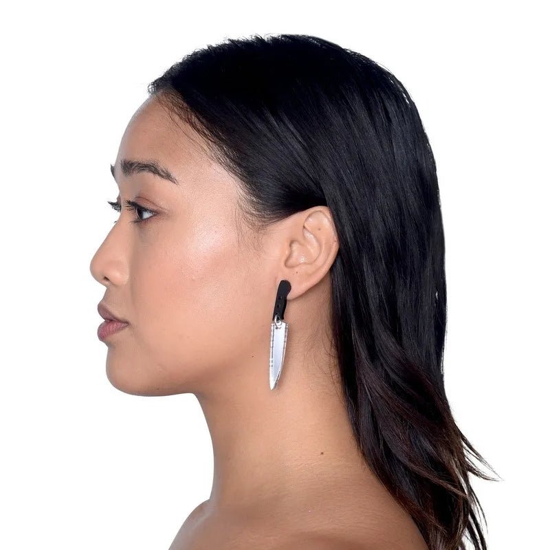 A woman with straight, dark hair is shown in profile against a white background, wearing Kiss Me Laters unique silver kitchen knife-shaped earrings hanging from her left ear.