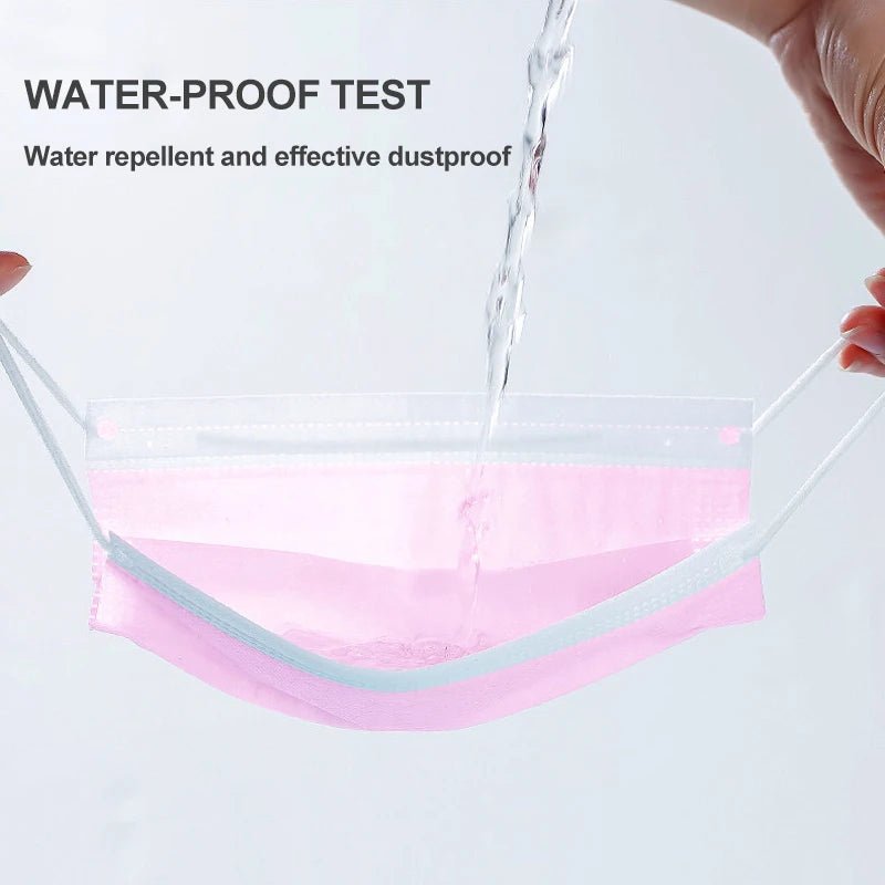 A stream of water is poured onto a Kiss Me Later pink triple layer mask, demonstrating its water repellent and dustproof qualities. Text on the image: WATER-PROOF TEST: Water repellent and effective dustproof.