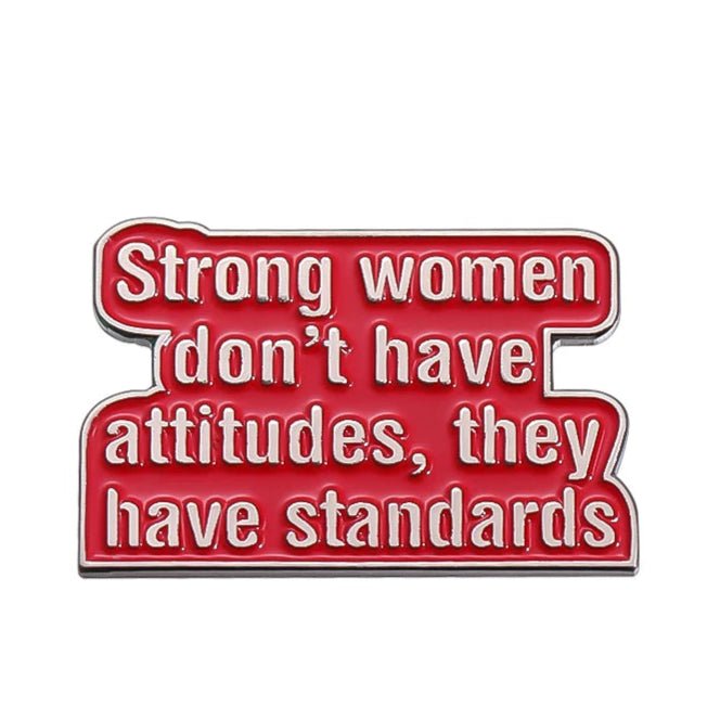 A red enamel pin by My Cutesy Era with white text: Strong women don’t have attitudes, they have standards. Perfect for empowered women gifts or any fan of feminist enamel pins.