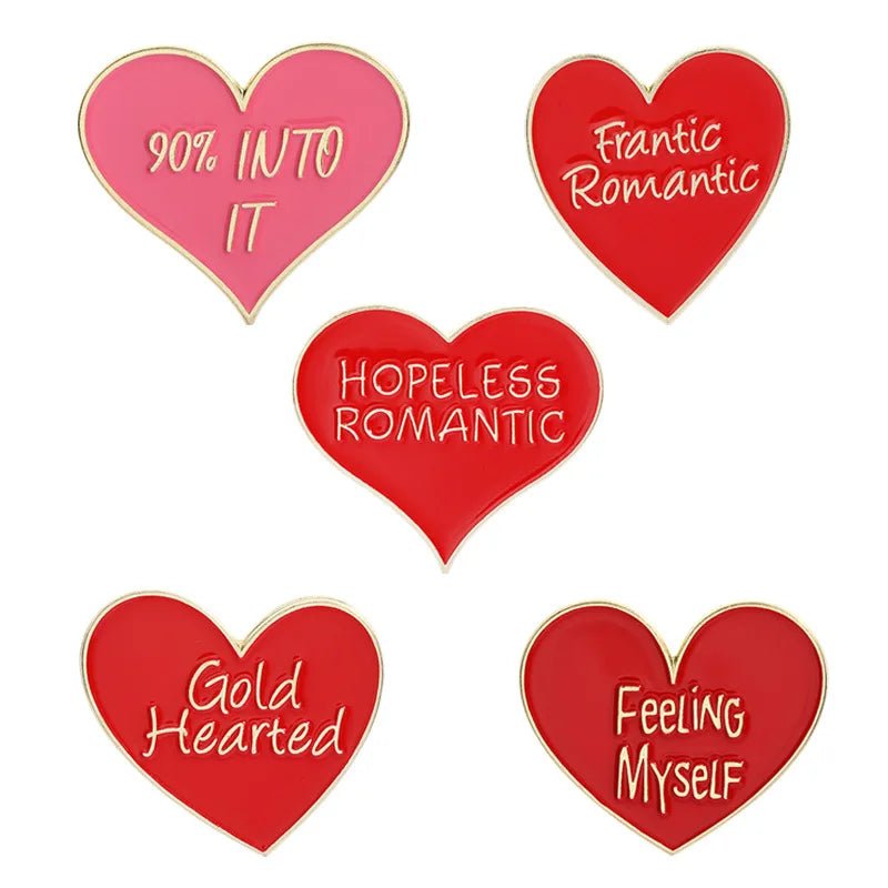 Five heart-shaped enamel pins: 90% Into It (pink), Frantic Romantic, Hopeless Romantic, Gold Hearted, and Feeling Myself (red). Each features gold trim, white text, and stylish red or pink enamel.