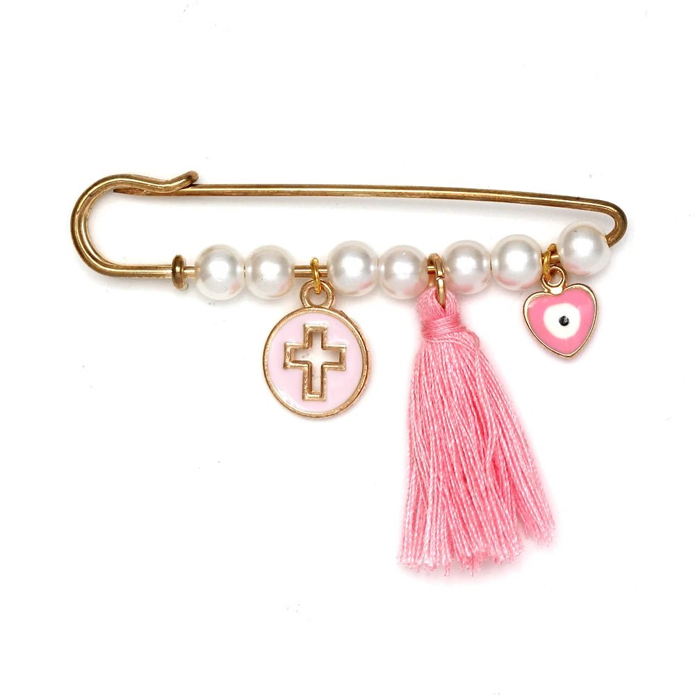 The Kiss Me Later gold safety pin brooch features white beads, a pink cross charm, a pink tassel, and a pink heart charm with an eye design—an adorable gift idea for baby showers.