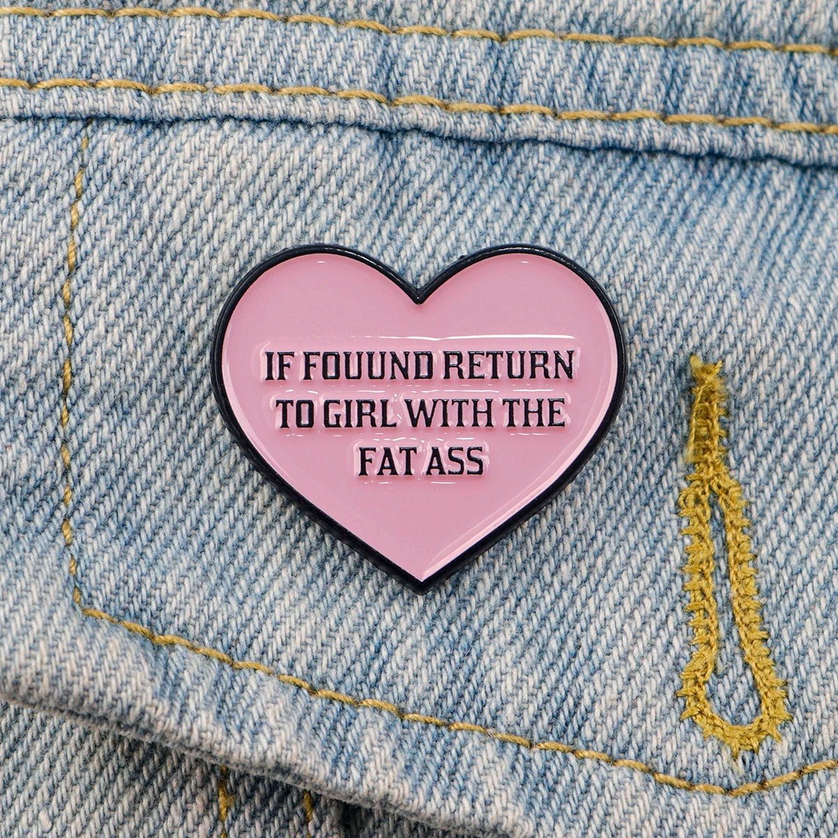 The Kiss Me Later pink heart enamel pin on denim states IF FOUND RETURN TO GIRL WITH THE FAT ASS in bold black letters—a cheeky, fun novelty accessory perfect for making a bold statement.