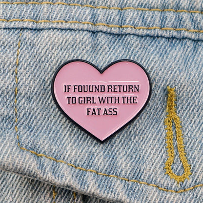The Kiss Me Later pink heart enamel pin on denim states IF FOUND RETURN TO GIRL WITH THE FAT ASS in bold black letters—a cheeky, fun novelty accessory perfect for making a bold statement.