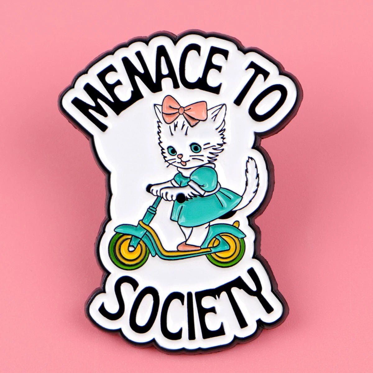 cat enamel pin shows a cute white kitten in a teal dress and pink bow riding a green scooter, with “MENACE TO SOCIETY” in bold black text on a pink background.