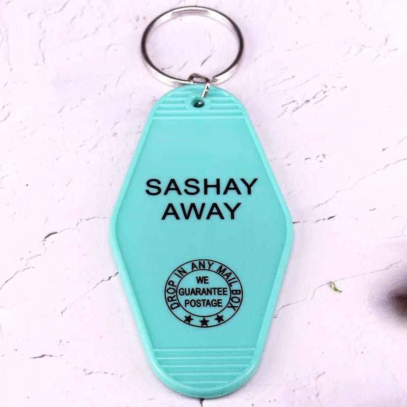 A teal retro hotel key ring by Kiss Me Later featuring “SASHAY AWAY” in black and a round stamp reading DROP IN ANY MAIL BOX WE GUARANTEE POSTAGE. Perfect for pop culture fans who love unique, colorful key rings.