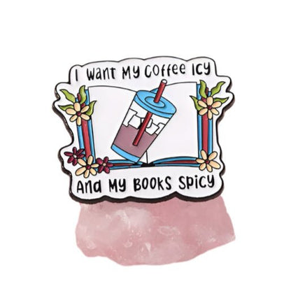 The My Cutesy Era enamel book pin shows flowers, books, and an iced coffee cup with the quote “I want my coffee icy and my books spicy.” Perfect for book lovers and bookworm gifts, it's displayed on a pink stone.