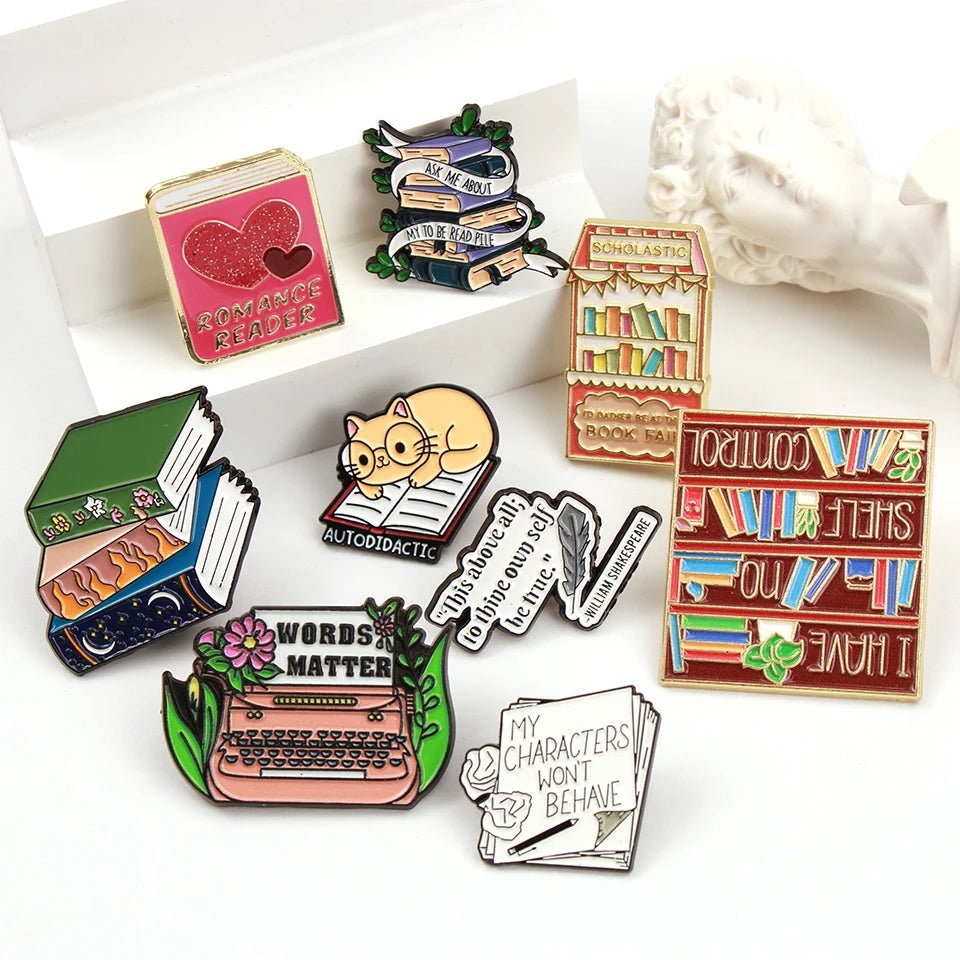 Badge collection features colorful book lover badges and enamel pins with cats, books, typewriters, “WORDS MATTER,” “MY CHARACTERS WON’T BEHAVE,” and a pink “ROMANCE READER” book.