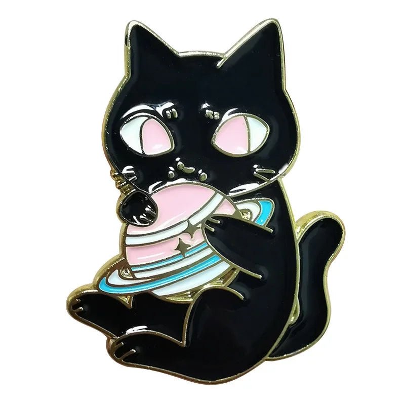 A whimsical Kiss Me Later black cat metal pin features large pink eyes and holds a pink-and-blue ringed planet, all outlined in gold—perfect for fans of playful, trendy accessories.