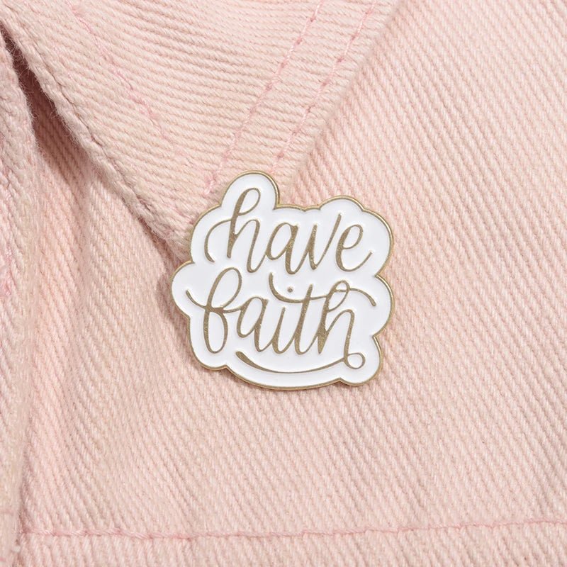 A white enamel pin with gold trim  featuring have faith in cursive, is attached to textured light pink fabric—a subtle, Bible-inspired reminder.