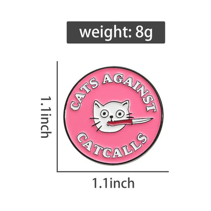 Round pink enamel pin features a white cat face holding a knife, surrounded by Cats Against Catcalls. This feminist badge measures 1.1 x 1.1 and weighs 8g.