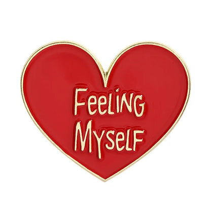 Heart-shaped enamel pin features a bold red and gold design, outlined in gold, with FEELING MYSELF in playful gold text at the center.