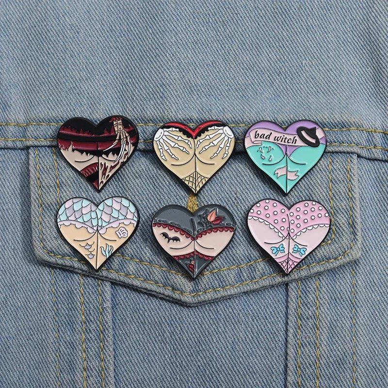Six heart-shaped enamel pins  featuring witch-themed gothic designs and unique illustrations of hands, hats, webs, fishnets, and enchanting patterns, are displayed on the back pocket of blue denim jeans.