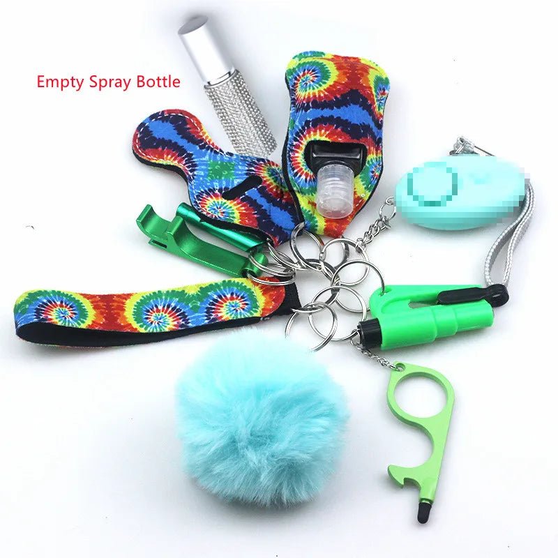 The Kiss Me Later colorful keychain set includes outdoor safety accessories: a tie-dye holder, green no-touch tool, blue pom-pom, whistle, teal alarm, and an empty spray bottle—perfect for adventures.