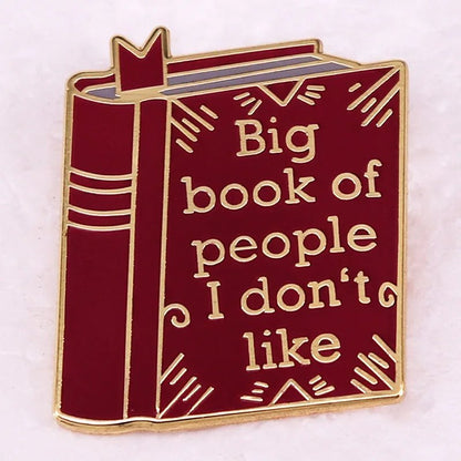 Red enamel pin is shaped like a book with gold outlines and the phrase Big book of people I dont like—a witty, playful accessory for romance readers or anyone who loves unique bookish badges.
