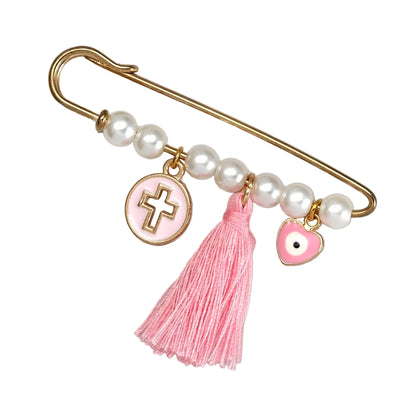 The Kiss Me Later gold safety pin brooch features white pearls, a pink tassel, a pink enamel cross charm, and a pink heart evil eye—making it an ideal baby shower gift. Shown on a white background.