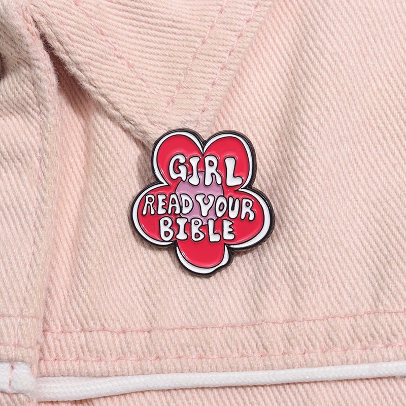 A pink and white flower enamel pin  sits on light pink fabric, with bold playful lettering that says GIRL READ YOUR BIBLE—a cute reminder to open your Bible every day.