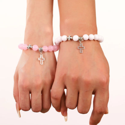 Two hands display Kiss Me Later crystal bead bracelets with cross pendants—one pink, one white. These Christian stone bracelets accent manicured nails against a light background.