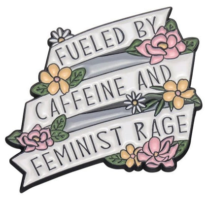 enamel pin features a white ribbon banner with Fueled by caffeine and feminist rage, accented with pink and yellow flowers, green leaves, and a tiny heart for a touch of self love.