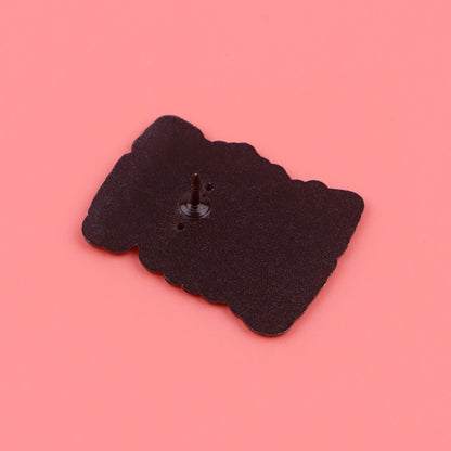 A Kiss Me Later black skeleton hand enamel pin with a single post and back clasp lies face down on a solid pink background, bringing subtle spooky vibes to your collection.