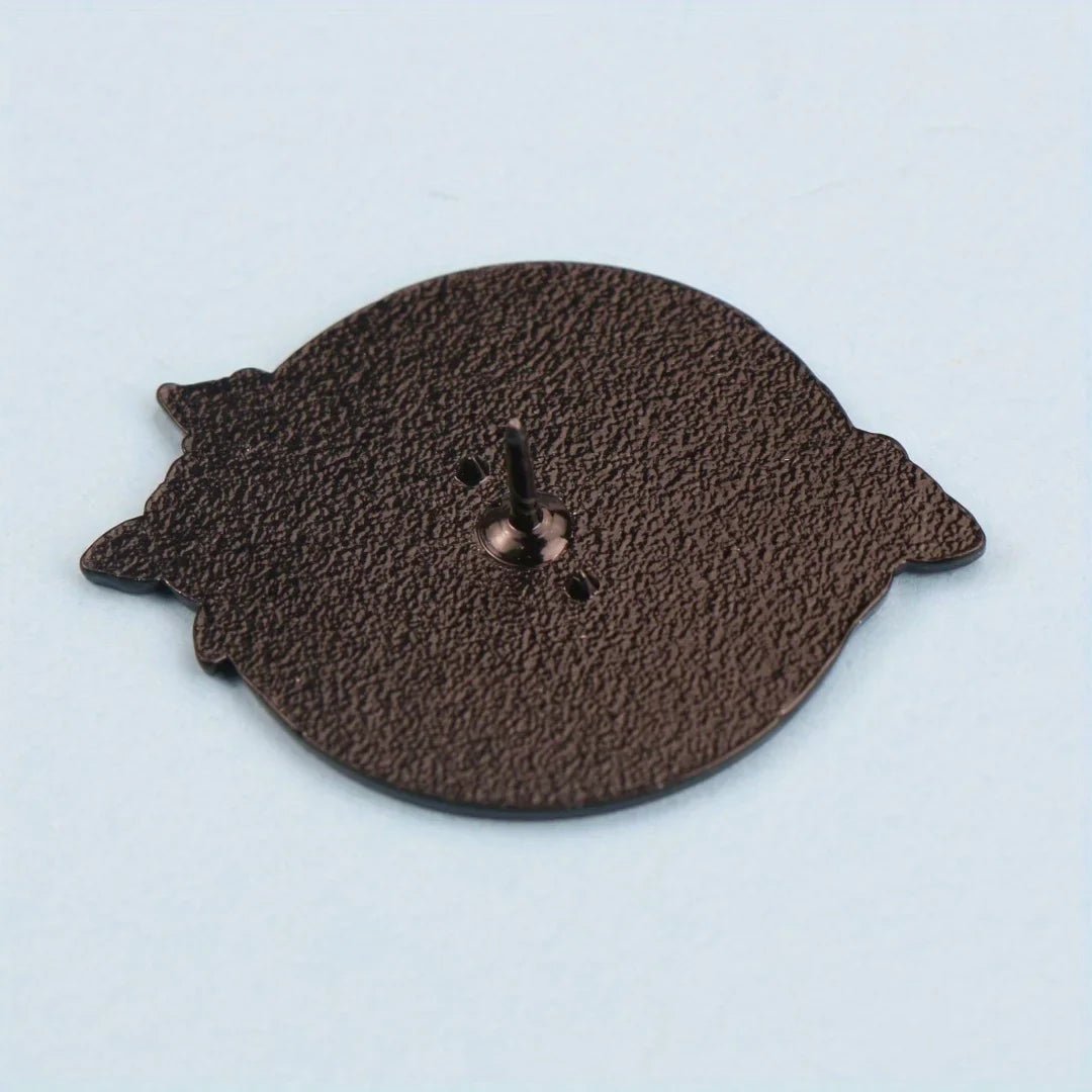 A round, textured, dark-colored skull enamel pin back from Gay Skate, featuring a central pin and two small side protrusions, displayed on a light blue background.