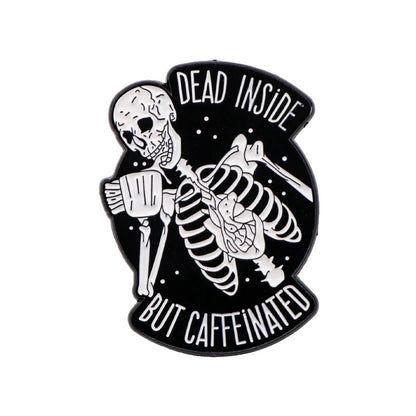 The Kiss Me Later enamel pin features a grinning skeleton holding a coffee mug on a black background with white stars. It reads DEAD INSIDE BUT CAFFEINATED—perfect for spooky vibes and coffee lovers!.