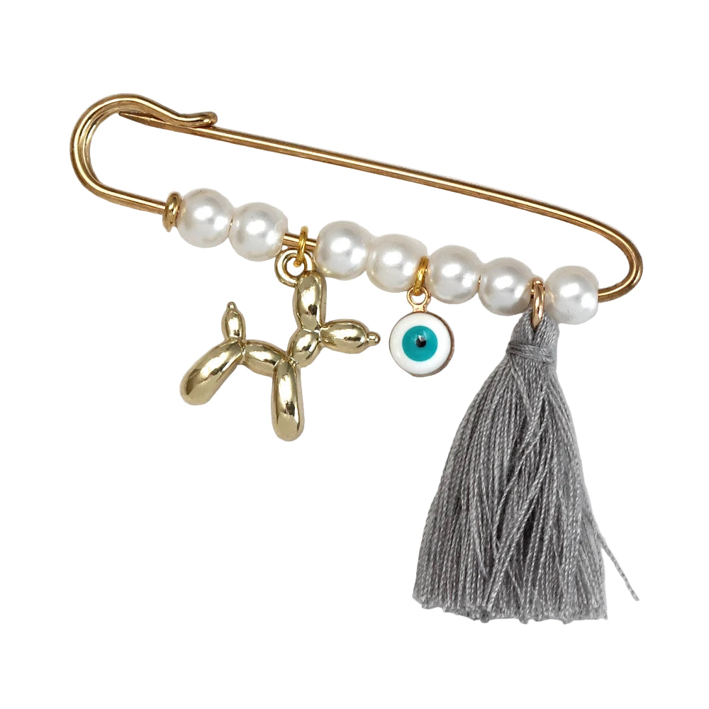 The Kiss Me Later gold brooch features four pearl beads, a gold balloon dog charm, an evil eye pin, and a gray tassel—an ideal baby shower gift, presented on light fabric.