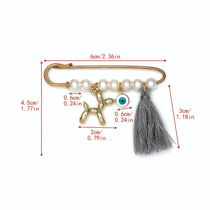 The Kiss Me Later gold safety pin features white pearls, a gold flower charm, blue evil eye charm, and gray tassel. Measuring 6cm x 4.5cm with a 3cm tassel, it’s an elegant brooch—perfect as a thoughtful baby shower gift.