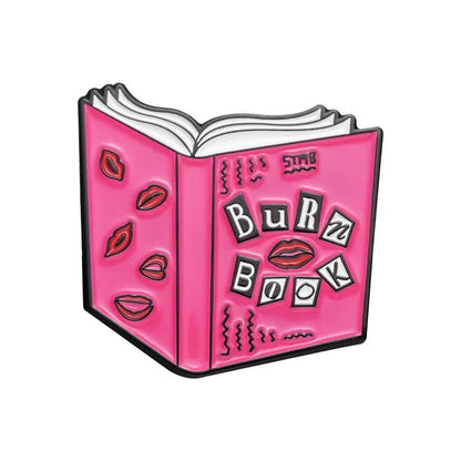 Illustration of an open pink book titled Burn Book with ransom note-style letters, red lipstick kiss marks, and a pink rollerskate pin—perfect enamel pin for Mean Girls fans from My Cutesy Era