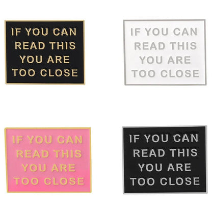 Four rectangular enamel pins from My Cutesy Era with IF YOU CAN READ THIS YOU ARE TOO CLOSE in caps, on black, white, pink, and black-with-white-border backgrounds. A funny lapel pin for any outfit.