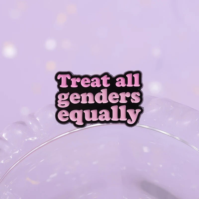 Enamel pin features bold pink and black text reading Treat all genders equally on a soft purple background—an empowering addition to any feminist pin collection.