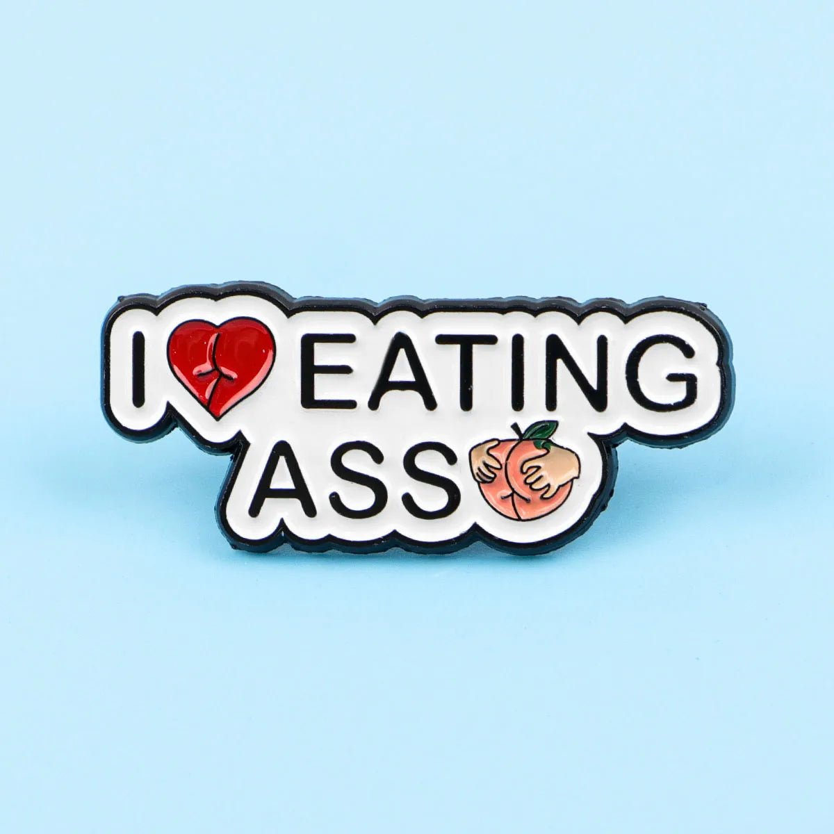 Kiss Me Later peach pin (3.5cm x 1.5cm) features “I Love Eating Ass” with a red heart for “love,” a peach and two hands for “ass,” all on a light blue background.