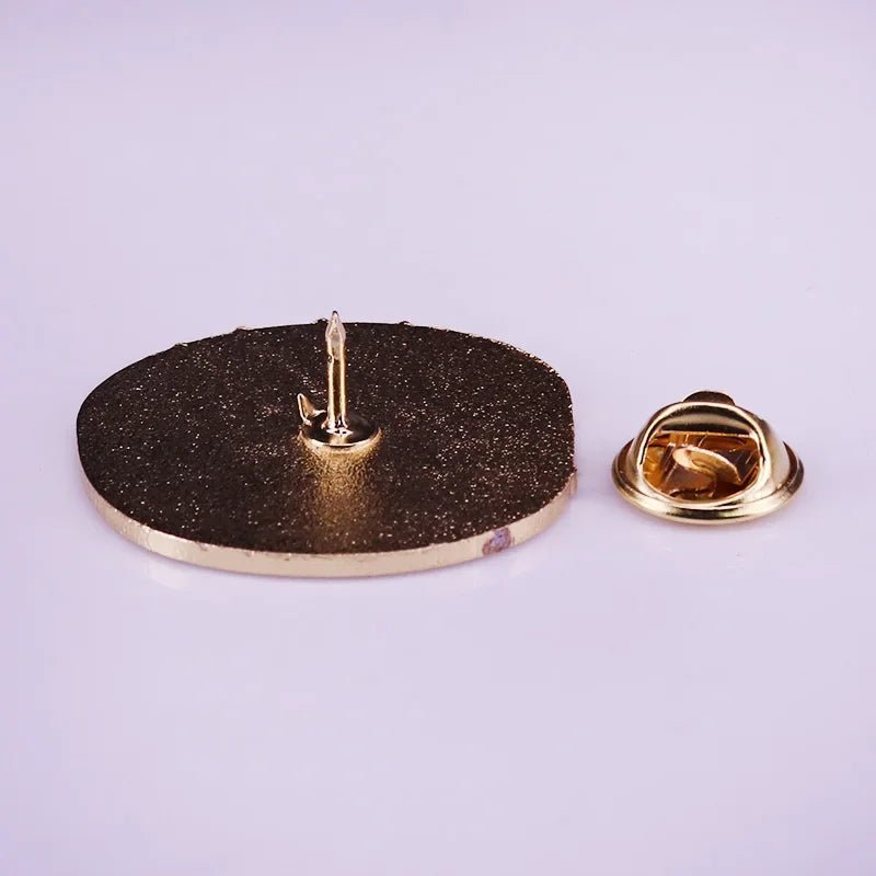 A My Cutesy Era gold enamel pin badge with a textured, round face lies flat on a light surface, its pointy pin and separate gold butterfly clutch backing displayed beside it.