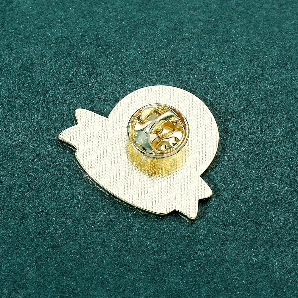 A gold ghost-shaped pin with a butterfly clasp rests on a textured dark green surface—an enchanting addition to any Pokémon enamel pin collection.