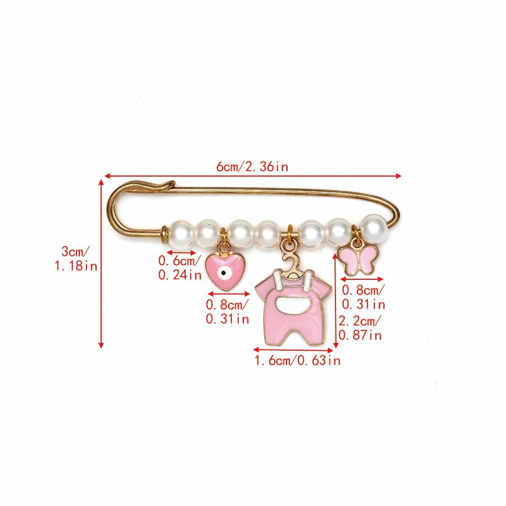 The Kiss Me Later gold safety pin features six pearls and three pink charms—a heart, overalls, and butterfly—creating a charming brooch. Red measurement lines indicate size in cm and inches; perfect as a baby shower gift.