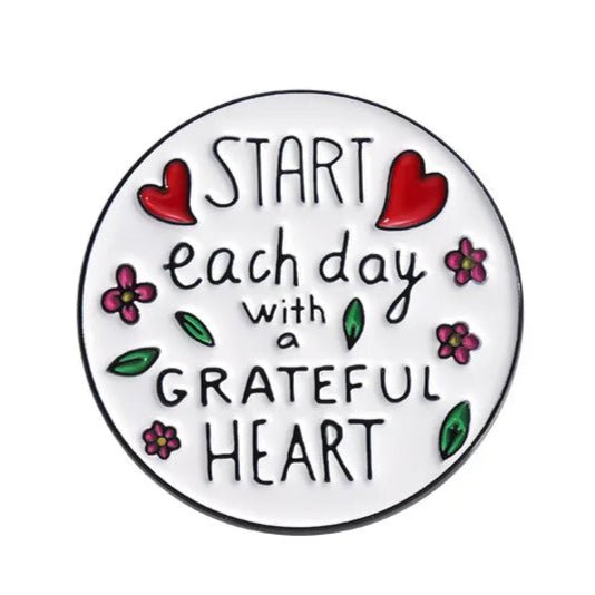 A round My Cutesy Era sign features red hearts, pink flowers, and green leaves on a white background with black handwritten-style text: Start each day with a grateful heart—inspiring décor for motivational enamel pin fans.