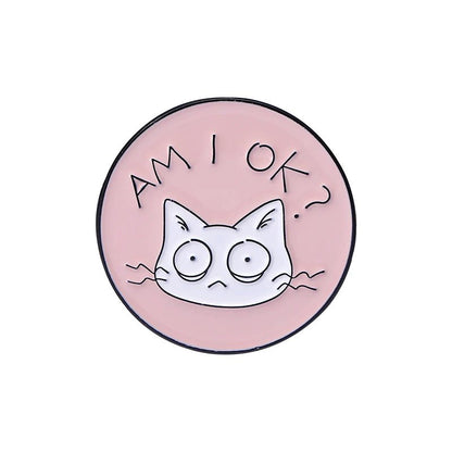 Round pink cat pin shows a wide-eyed cartoon feline with AM I OK? above its head. This quirky accessory features an anxious cat, adding charm and personality to your style.
