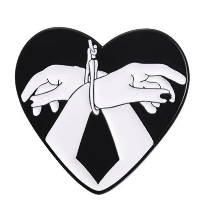 The heart-shaped image from My Cutesy Era shows two bound hands in bold black and white on a dark background—an ideal love heart or bound hands enamel pin full of striking contrast and deep emotion.