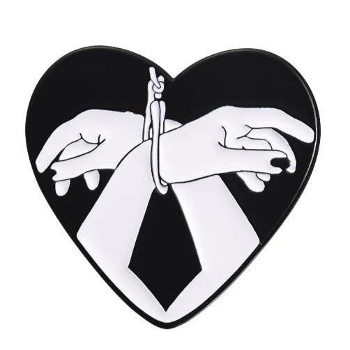 The heart-shaped image from My Cutesy Era shows two bound hands in bold black and white on a dark background—an ideal love heart or bound hands enamel pin full of striking contrast and deep emotion.