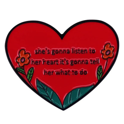 Express your unique style with the My Cutesy Era red enamel heart pin, adorned with flowers and green leaves. The center reads: shes gonna listen to her heart its gonna tell her what to do—a cute pink love heart accessory.