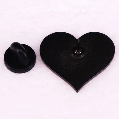 A 1-inch black heart-shaped enamel pin shown with its butterfly clutch backing detached on a white surface.