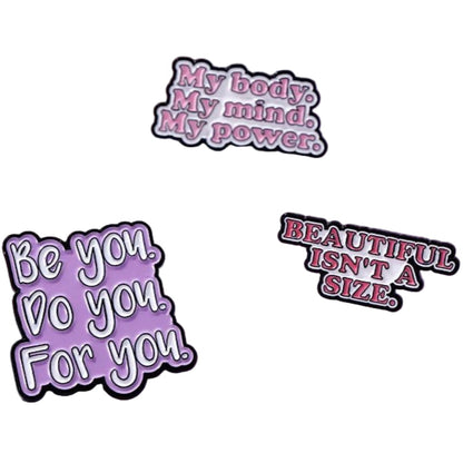  three enamel pins celebrate self-love with empowering phrases like “Be you. Do you. For you.”—displayed on a pink and white surface next to a flamingo image, each radiating confidence.