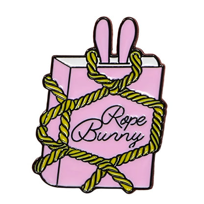 The My Cutesy Era Rope Bunny enamel pin features a pink rectangle with bunny ears wrapped in yellow rope and cursive text on the front—a charming addition to any collection.