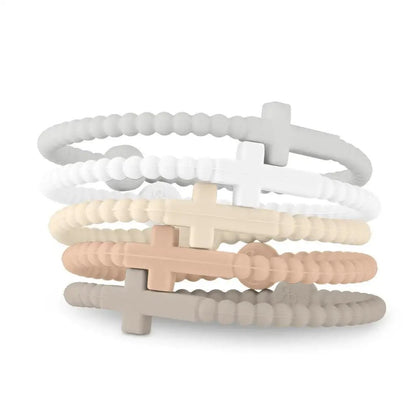 Five Kiss Me Later Cutie Bracelets in neutral tones—white, light gray, beige, tan, and taupe—are stacked together on a white background. Each features a beaded design with a cross charm inspired by Jesus.
